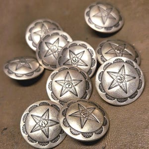 May include: A collection of silver-toned metal buttons. Each button features a star design with the letter "W" in the center, surrounded by a scalloped edge. The buttons are likely for decorative purposes.