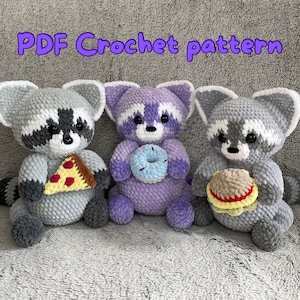 May include: Three crocheted raccoon amigurumi toys, each holding a different food item: a slice of pizza, a donut, and a hamburger. The toys are gray, purple, and gray with white accents. The image includes the text "PDF Crochet pattern".