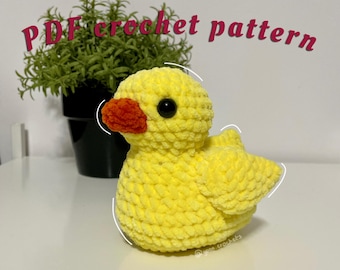 May include: A yellow crocheted duck with a red beak and black eyes. The duck is sitting on a white surface. The text "PDF crochet pattern" is written in pink above the duck.