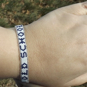 Könnte beinhalten: Ein weißes und blaues Freundschaftsarmband mit dem Wort "HOOCH" in das Design eingewebt.