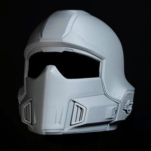Könnte beinhalten: Hellgrauer Helm im futuristischen Stil mit großem Visier und detaillierter Frontplatte. Der Helm hat eine glatte, matte Oberfläche und ist mit kantigen Linien und Belüftungsöffnungen versehen.