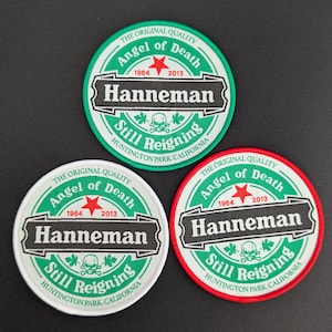 Op de afbeelding: Drie ronde patches met de tekst "Angel of Death" en "Hanneman". De patches hebben een witte rand, met groene en rode accenten. De tekst "Still Reigning" en "Huntington Park, California" is ook zichtbaar.