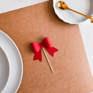May include: A red paper bow tied with a wooden stick, on a brown paper background.