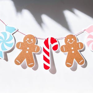 May include: A festive Christmas garland with gingerbread men, candy canes, and peppermint candies. The garland is strung with red string and is perfect for decorating a home or party.