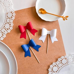 May include: Three paper bows on sticks, red, white, and blue, on a brown background.