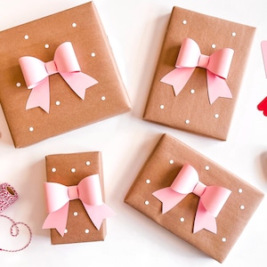 May include: Four brown gift boxes with pink paper bows and white polka dots. The boxes are on a white surface with pink and red gift tags.