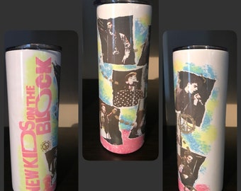May include: White stainless steel tumbler with a colorful design featuring images of the band New Kids on the Block. The text "New Kids on the Block" is printed in pink and black on the side of the tumbler.