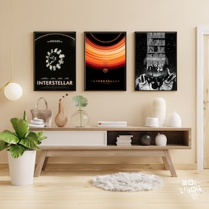 Può includere: Tre poster di film incorniciati in nero con il titolo "Interstellar" su una parete beige sopra uno scaffale in legno con un vaso bianco, un vaso marrone e un vaso di vetro trasparente con una pianta verde. Lo scaffale è sopra un mobile TV in legno marrone chiaro con un cassetto bianco e ripiani aperti. Il mobile TV è su un pavimento in legno chiaro con un tappeto bianco e soffice di fronte.