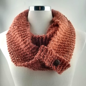 May include: A rust-colored knitted infinity scarf with a brown button. The scarf is made of a soft, fuzzy yarn and is perfect for keeping warm in the winter.