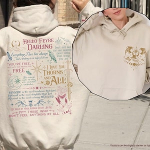 May include: A cream-colored hoodie with a graphic print featuring a quote from the book A Court of Thorns and Roses. The quote reads "Hello Feyre Darling, Everything I have always had a tendency to be taken from me. You're free. Not safe, not protected. Free. We need to remember we cannot endure..." The graphic also includes a raven, a sword, and a crown.
