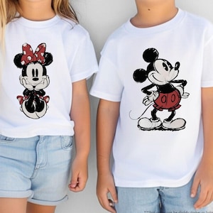 May include: Two children wearing white t-shirts with Disney character graphics. One shirt features Minnie Mouse with a red polka dot bow, and the other features Mickey Mouse in a red outfit. Both are wearing sunglasses.