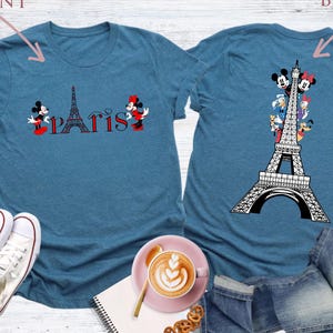 Pu&ograve; includere: T-shirt color turchese con grafica della Torre Eiffel e la scritta "Parigi". La parte anteriore della maglietta presenta Topolino e Minnie. Il retro della maglietta presenta la Torre Eiffel con vari personaggi dei cartoni animati.