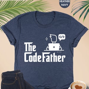 May include: A heather navy blue t-shirt with a white graphic of a person sitting at a computer with the text "The Code Father" and code symbols.