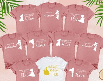 Puede incluir: Conjunto de nueve camisetas con un tema de princesas Disney con textos como "Hakuna Moscato, significa más vino" y "Lo suficientemente valiente para un trago". Una camiseta blanca presenta una corona dorada y el texto "Bibbidi Bobbidi I Do".