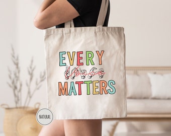 May include: A white tote bag with the text "EVERY VOICE MATTERS" in colorful letters. The text is in American Sign Language.