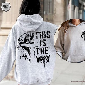 May include: A gray hooded sweatshirt with a black graphic print of a Mandalorian helmet and the text "This is the Way".
