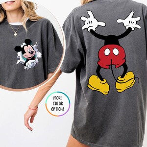 May include: Dark grey t-shirt featuring Mickey Mouse. The front has a circular graphic of Mickey bursting through a torn design. The back displays a large Mickey Mouse graphic with white gloves, red shorts, and yellow shoes. The word "PEPPER" is in the upper right corner.