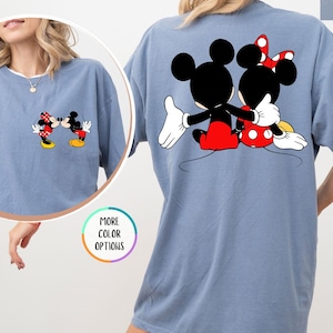 May include: Blue jean coloured t-shirt featuring a graphic of Mickey and Minnie Mouse. The front of the shirt shows the characters facing each other, while the back displays them embracing. The shirt has a relaxed fit.