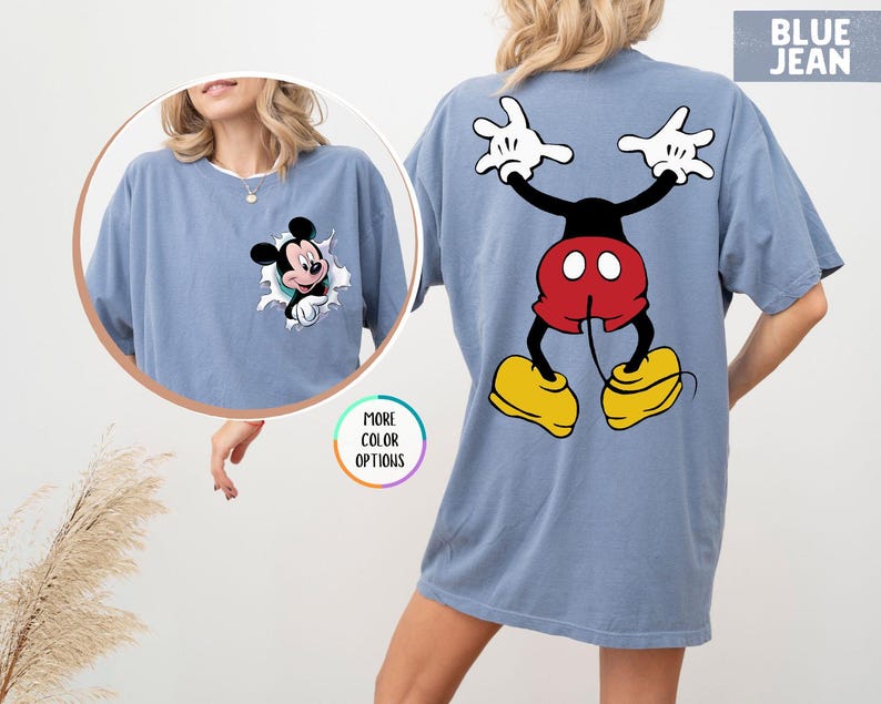 May include: Blue jean coloured t-shirt featuring Mickey Mouse. The front of the shirt has a graphic of Mickey Mouse bursting through a hole. The back of the shirt has a large graphic of Mickey Mouse with his arms up and his legs spread.