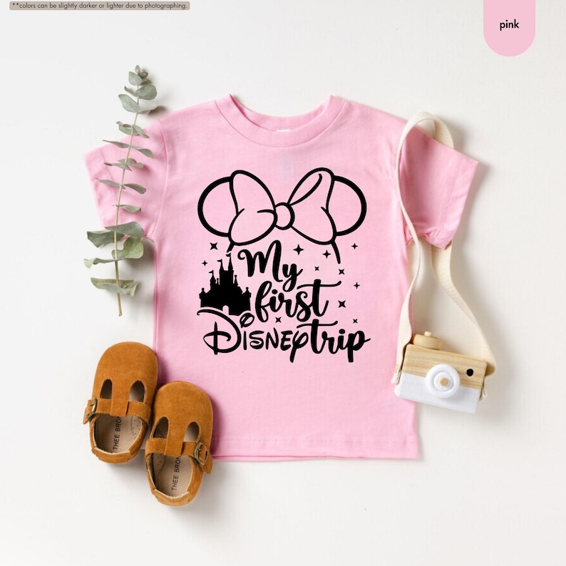 Pu&ograve; includere: Maglietta rosa a maniche corte con una grafica nera di orecchie di Topolino con un fiocco, un castello e il testo "My first Disney trip".