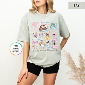 May include: A light green t-shirt featuring a colorful graphic of various Disney characters and icons. The text "Walt Disney World" and "The Most Magical Place on Earth" are also displayed. The shirt has short sleeves and a relaxed fit.