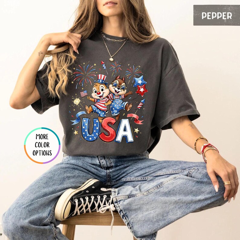 May include: Dark gray t-shirt featuring a patriotic design with the word "USA" in red, white, and blue. The graphic includes cartoon chipmunks, fireworks, and stars, celebrating the Fourth of July.