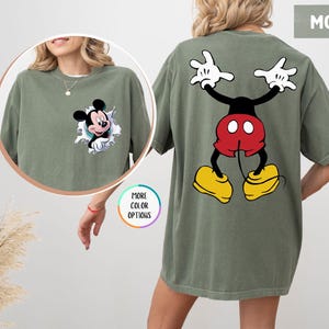 May include: Moss green t-shirt featuring Mickey Mouse. The front of the shirt shows Mickey bursting through a torn graphic. The back of the shirt displays Mickey in a playful pose. The shirt is a comfortable, oversized fit.