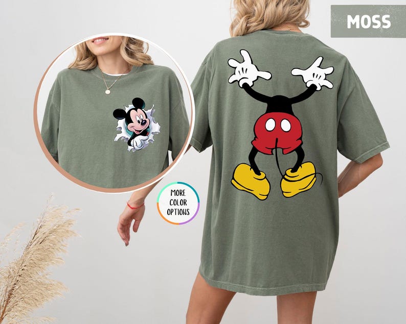 May include: Moss green t-shirt featuring Mickey Mouse. The front of the shirt shows Mickey bursting through a torn graphic. The back of the shirt displays Mickey in a playful pose. The shirt is a comfortable, oversized fit.