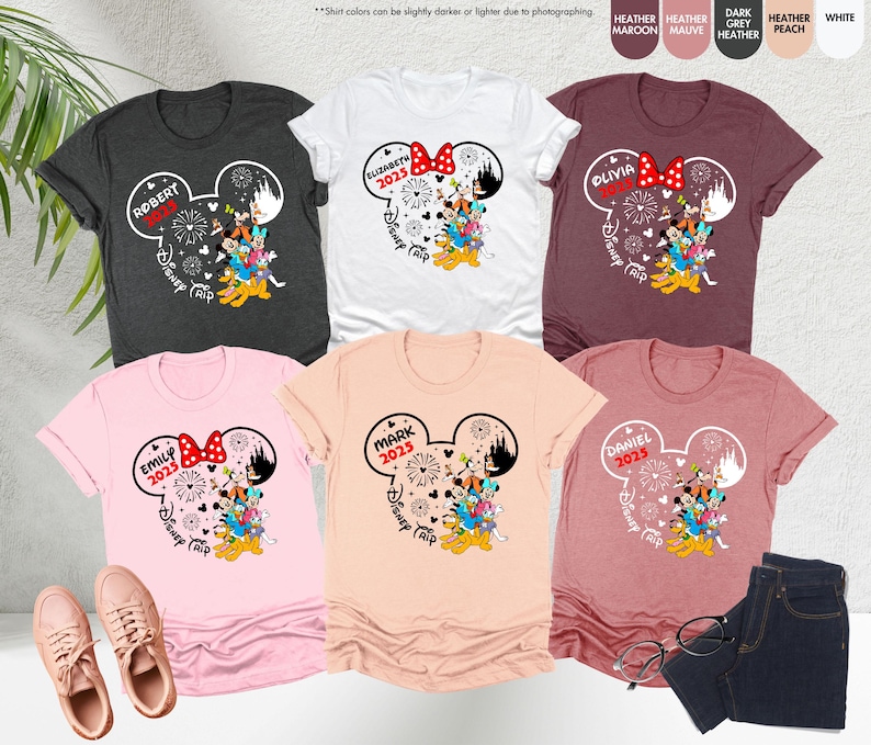 May include: Six t-shirts with a Mickey Mouse ear design featuring a family of Disney characters. Each shirt has a different name and the year 2025. The shirts are in various colors including heather grey, white, maroon, peach, pink, and light orange.