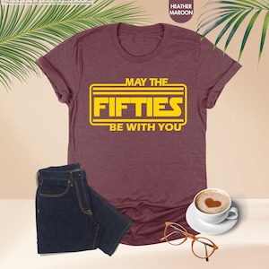 May include: A heather maroon t-shirt with a yellow graphic that says "May the Fifties Be With You".
