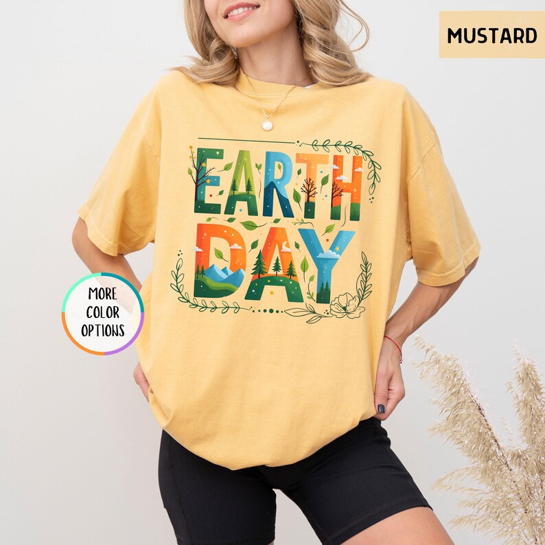 May include: A mustard yellow t-shirt with the words "Earth Day" in colorful letters surrounded by green leaves and flowers.