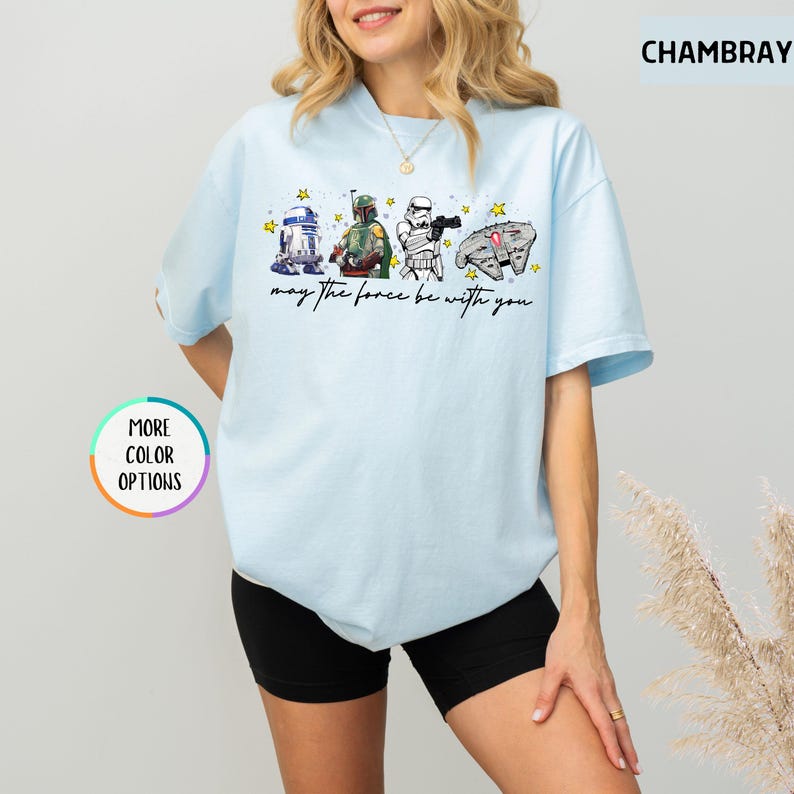 Puede incluir: Camiseta azul claro con personajes de Star Wars: R2-D2, Boba Fett, un Stormtrooper y el Halc&oacute;n Milenario. La frase "may the force be with you" est&aacute; impresa debajo. La camiseta tiene mangas cortas y cuello redondo.