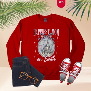 May include: A red sweatshirt with the text "HAPPIEST MOM on Earth" and a graphic of a castle. The image also includes a pair of blue jeans, red sneakers, and eyeglasses.