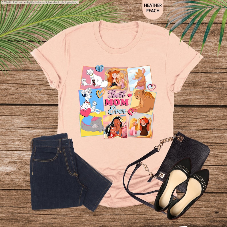 Pode incluir: Camiseta rosa com uma colagem de princesas e personagens da Disney, incluindo Ariel, Bela, Pocahontas e Simba. O texto "Best Mom Ever" est&aacute; no centro da colagem.