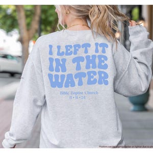 May include: Sport grey sweatshirt with the text "I LEFT IT IN THE WATER" in light blue, along with "Bible Baptist Church" and the date "11-11-24". The sweatshirt is a long-sleeved crew neck.
