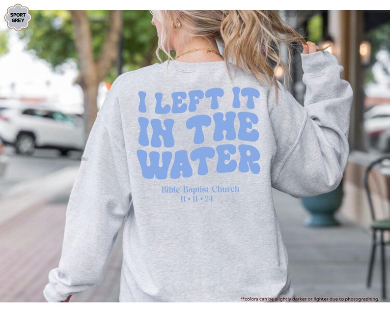 May include: Sport grey sweatshirt with the text "I LEFT IT IN THE WATER" in light blue, along with "Bible Baptist Church" and the date "11-11-24". The sweatshirt is a long-sleeved crew neck.