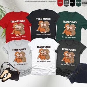Puede incluir: Una colecci&oacute;n de camisetas en varios colores, incluyendo rojo, negro y gris. Cada camiseta presenta el texto "TEAM PUNCH" sobre una ilustraci&oacute;n de dos monos abraz&aacute;ndose. La frase "You are never alone!" est&aacute; impresa debajo.