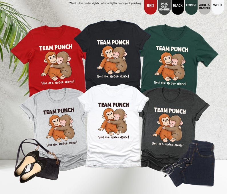 Puede incluir: Una colecci&oacute;n de camisetas en varios colores, incluyendo rojo, negro y gris. Cada camiseta presenta el texto "TEAM PUNCH" sobre una ilustraci&oacute;n de dos monos abraz&aacute;ndose. La frase "You are never alone!" est&aacute; impresa debajo.