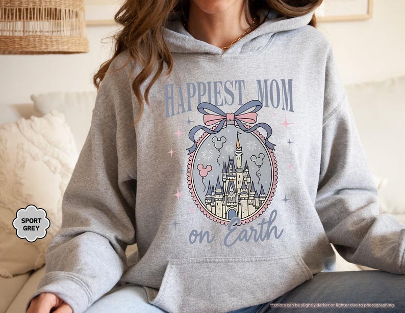 May include: Sport grey hoodie with a front graphic that reads "Happiest Mom on Earth." The graphic features a castle design with a pink and blue bow and Mickey Mouse balloons. The hoodie has a drawstring hood and a front pocket.