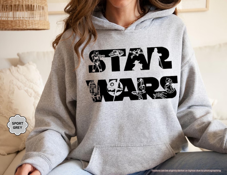 May include: A gray hooded sweatshirt with the text 'STAR WARS' in black letters. The text is surrounded by various Star Wars characters and objects, including Darth Vader, Yoda, R2-D2, and a TIE fighter.