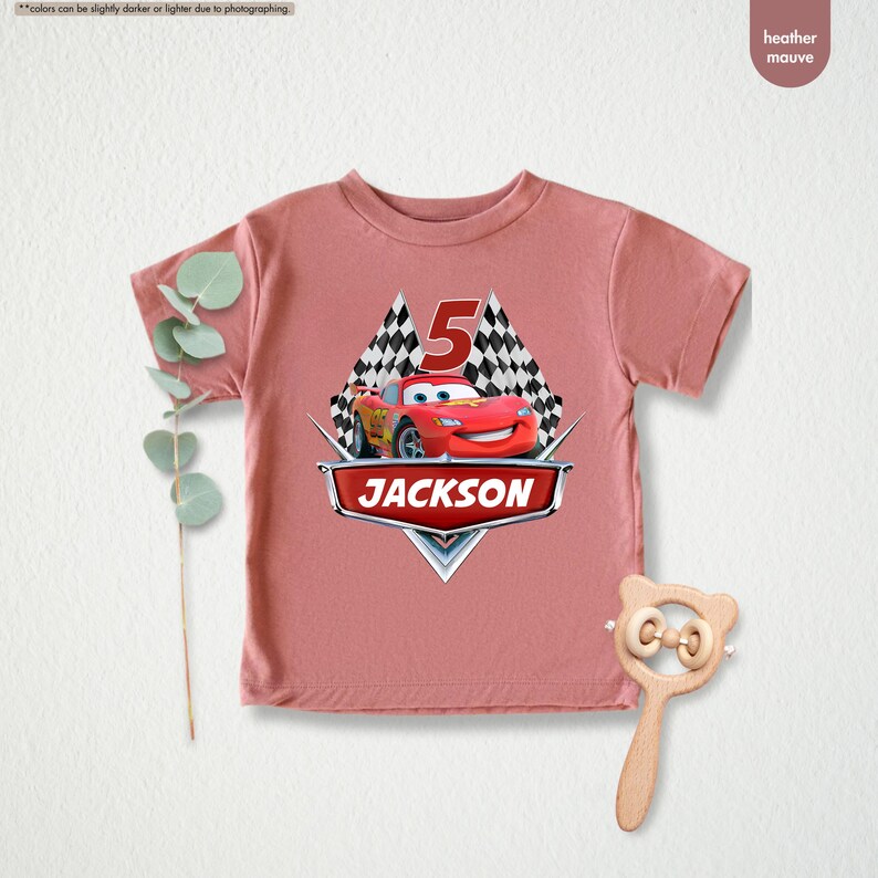 Op de afbeelding: Een heidepaars T-shirt met een rode raceauto-afbeelding en de tekst "JACKSON" en "5" erop gedrukt.