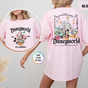 Puede incluir: Camiseta rosa claro con un dise&ntilde;o de Disneyworld. La parte delantera presenta el texto "Disneyworld Est. 1971 Florida" con Mickey, Minnie, Donald y Goofy. La parte trasera tiene un castillo y el texto "Disneyworld 1971".