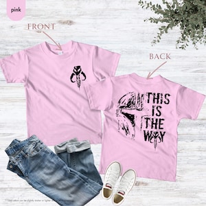 Pu&ograve; includere: Maglietta rosa con una grafica nera di un elmetto mandaloriano sul retro e un simbolo nero sul davanti. Il testo "This is the Way" &egrave; stampato sul retro della maglietta.