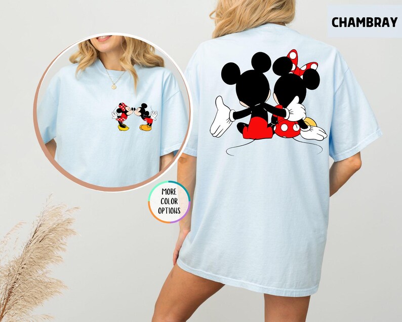 May include: Pale blue t-shirt with Mickey and Minnie Mouse graphics. The front shows the characters kissing, and the back has a larger image of them embracing. The word "CHAMBRAY" is printed on the top right of the t-shirt.