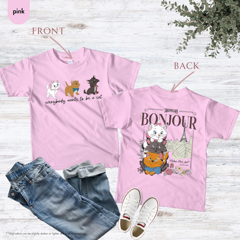 May include: Pink t-shirts with cat graphics. One shirt features three cartoon cats and the text "everybody wants to be a cat." The other shirt has a graphic of three cats with the Eiffel Tower and the word "Bonjour."