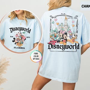 Puede incluir: Camiseta azul claro con un gr&aacute;fico de Disneyworld. La parte delantera presenta un dise&ntilde;o circular con personajes de Disney y el texto "Disneyworld Est. 1971 Florida". La parte trasera muestra un dise&ntilde;o m&aacute;s grande con personajes de Disney y un castillo.
