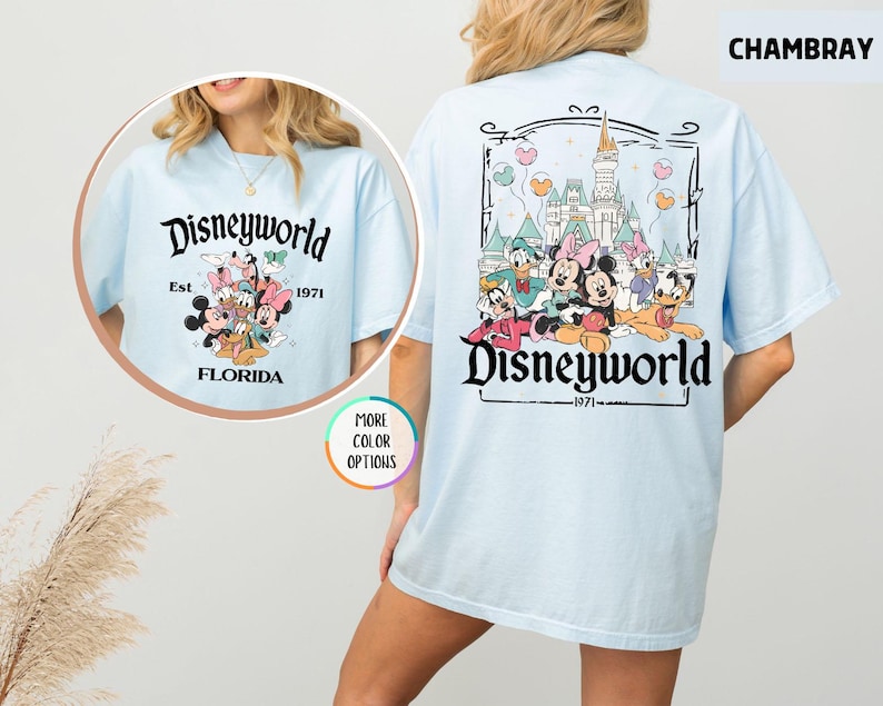 Puede incluir: Camiseta azul claro con un gr&aacute;fico de Disneyworld. La parte delantera presenta un dise&ntilde;o circular con personajes de Disney y el texto "Disneyworld Est. 1971 Florida". La parte trasera muestra un dise&ntilde;o m&aacute;s grande con personajes de Disney y un castillo.