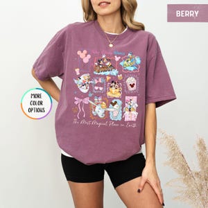 May include: Berry-colored t-shirt featuring a colorful graphic of Disney characters and attractions. The design includes images of Mickey and Minnie Mouse, Dumbo, and other iconic elements. Text on the shirt reads "Walt Disney World" and "The Most Magical Place on Earth."