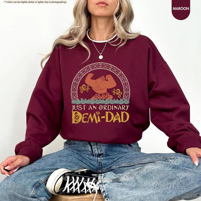 Puede incluir: Una sudadera color granate con un gr&aacute;fico de un personaje de dibujos animados y el texto "Just an ordinary Demi-Dad" impreso en la parte delantera.