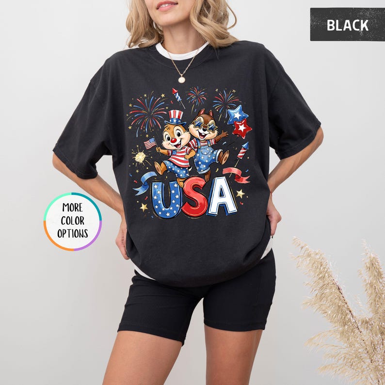 May include: Black t-shirt featuring a graphic of two cartoon chipmunks celebrating with fireworks and the word "USA". The chipmunks are wearing patriotic outfits. The shirt has a crew neck and short sleeves.